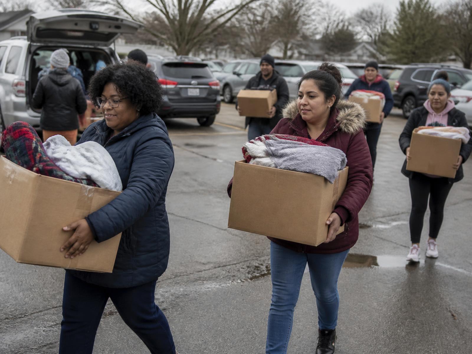 Community members carrying boxes of donated blankets and clothing
